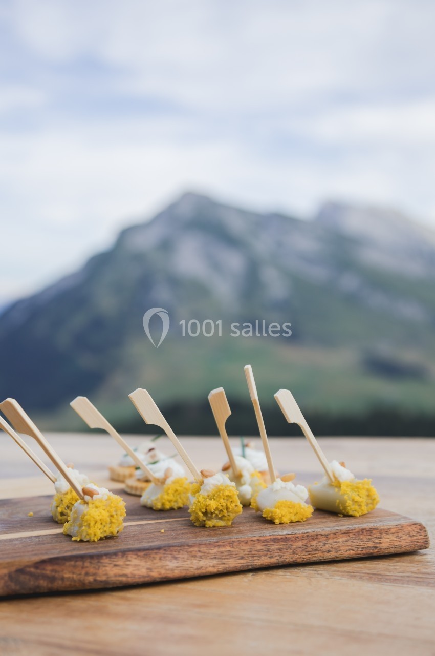 Amuse-bouches élégants présentés sur une planche en bois avec un paysage de montagne en arrière-plan.