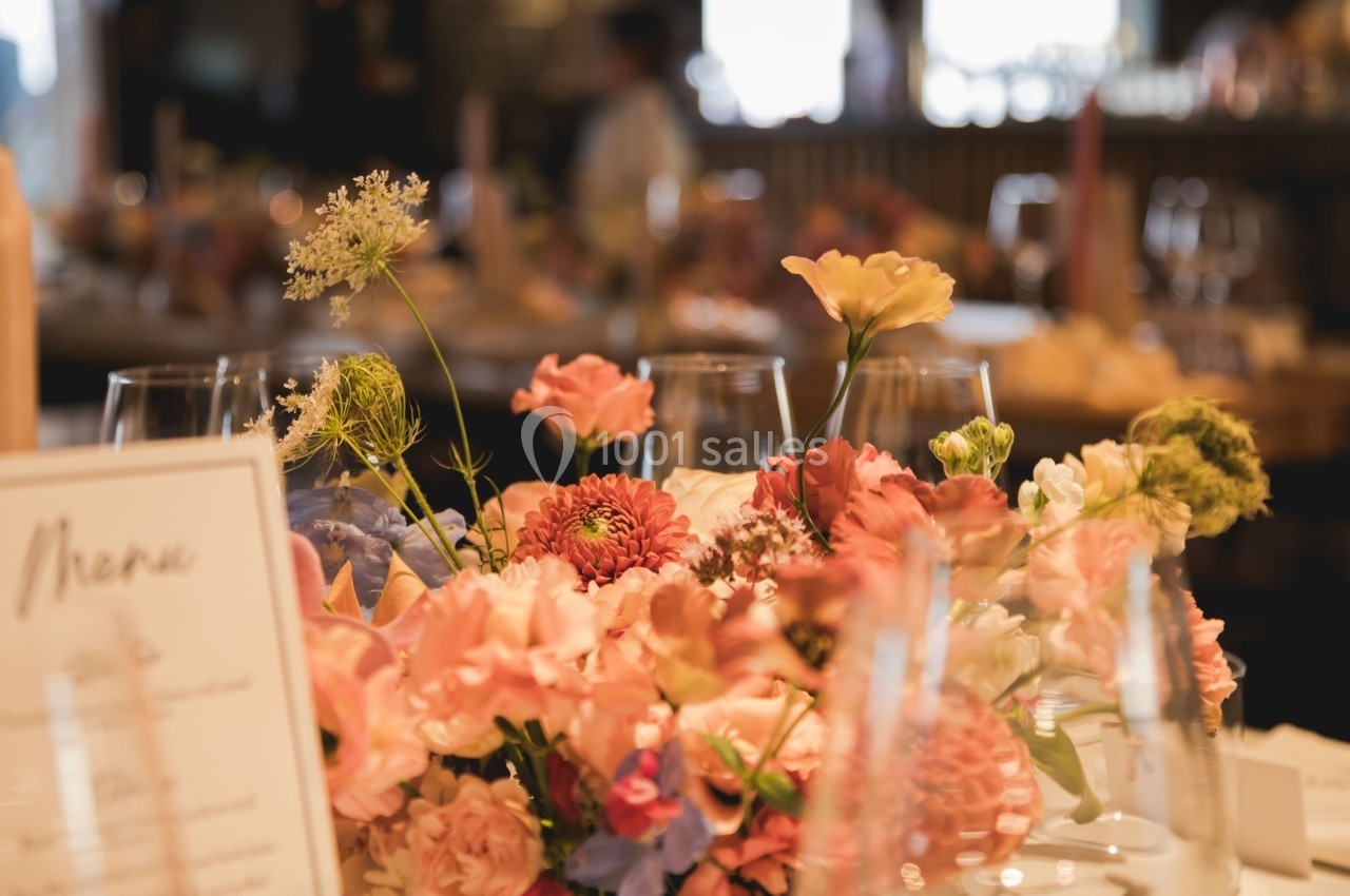 Arrangement floral coloré avec des fleurs roses, rouges et jaunes sur une table dressée dans un cadre lumineux.