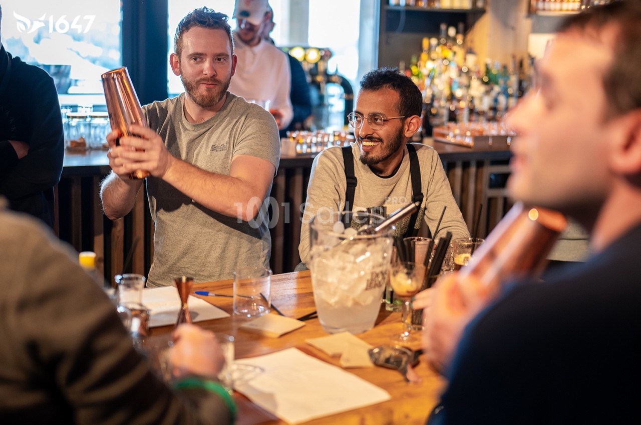 Des personnes participent à un atelier de mixologie dans un bar, préparant des cocktails avec des shakers et des ingrédients…