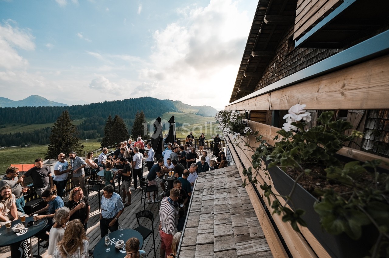Groupe de personnes rassemblées sur une terrasse en bois avec vue sur des montagnes et une vallée verdoyante.