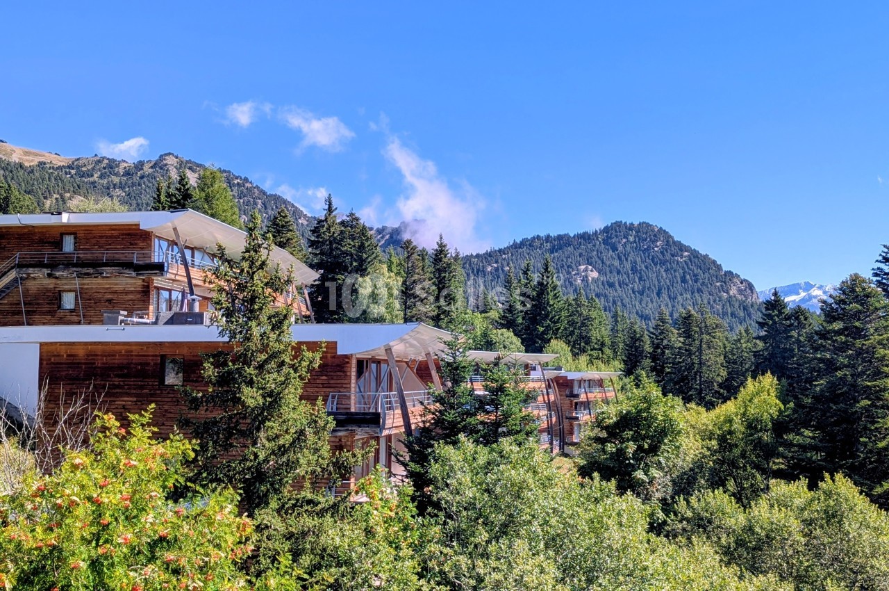 Chalets en bois entourés de forêts et montagnes sous un ciel bleu clair.