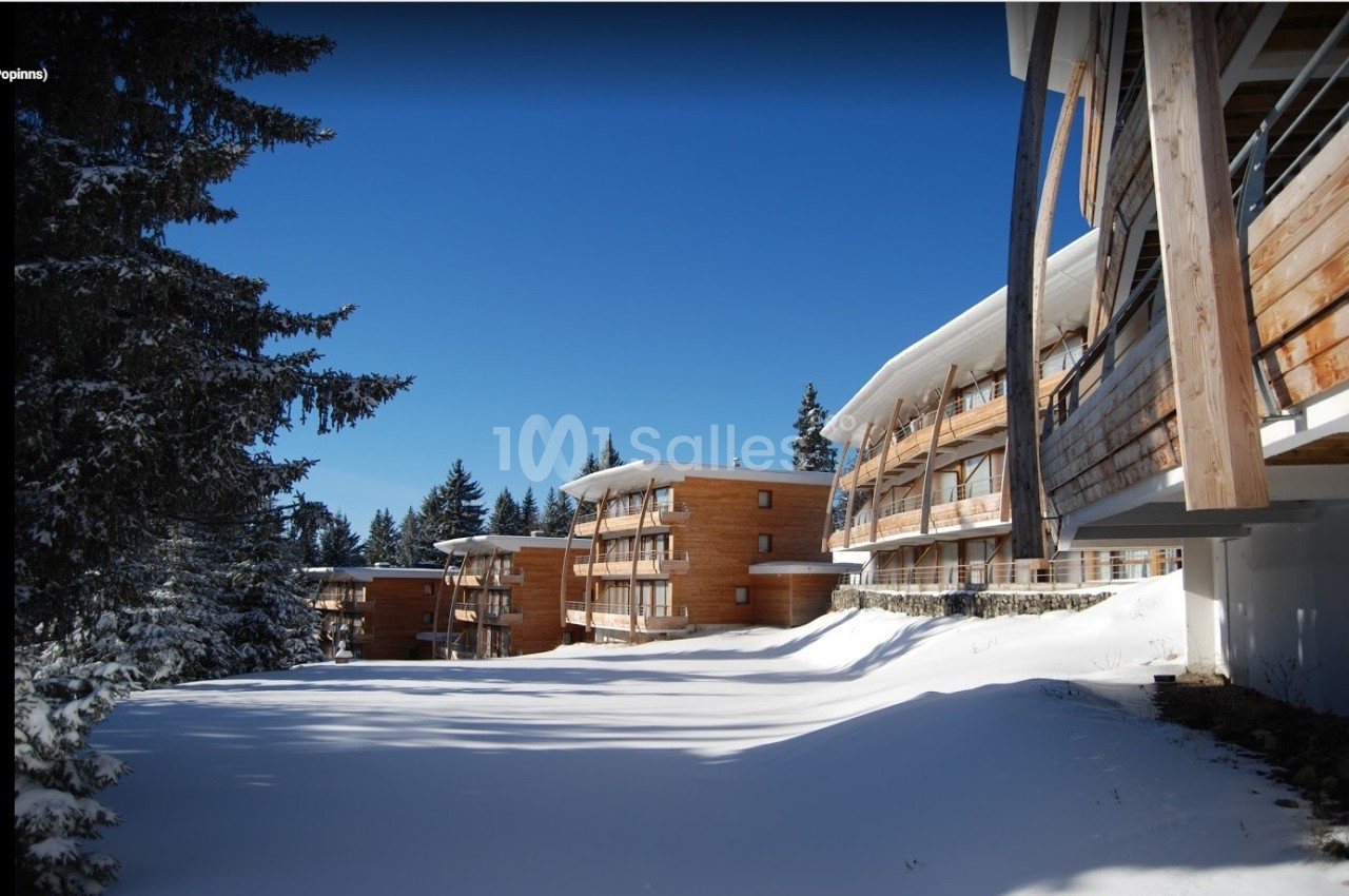 Bâtiments en bois modernes entourés de neige et de sapins sous un ciel bleu clair.