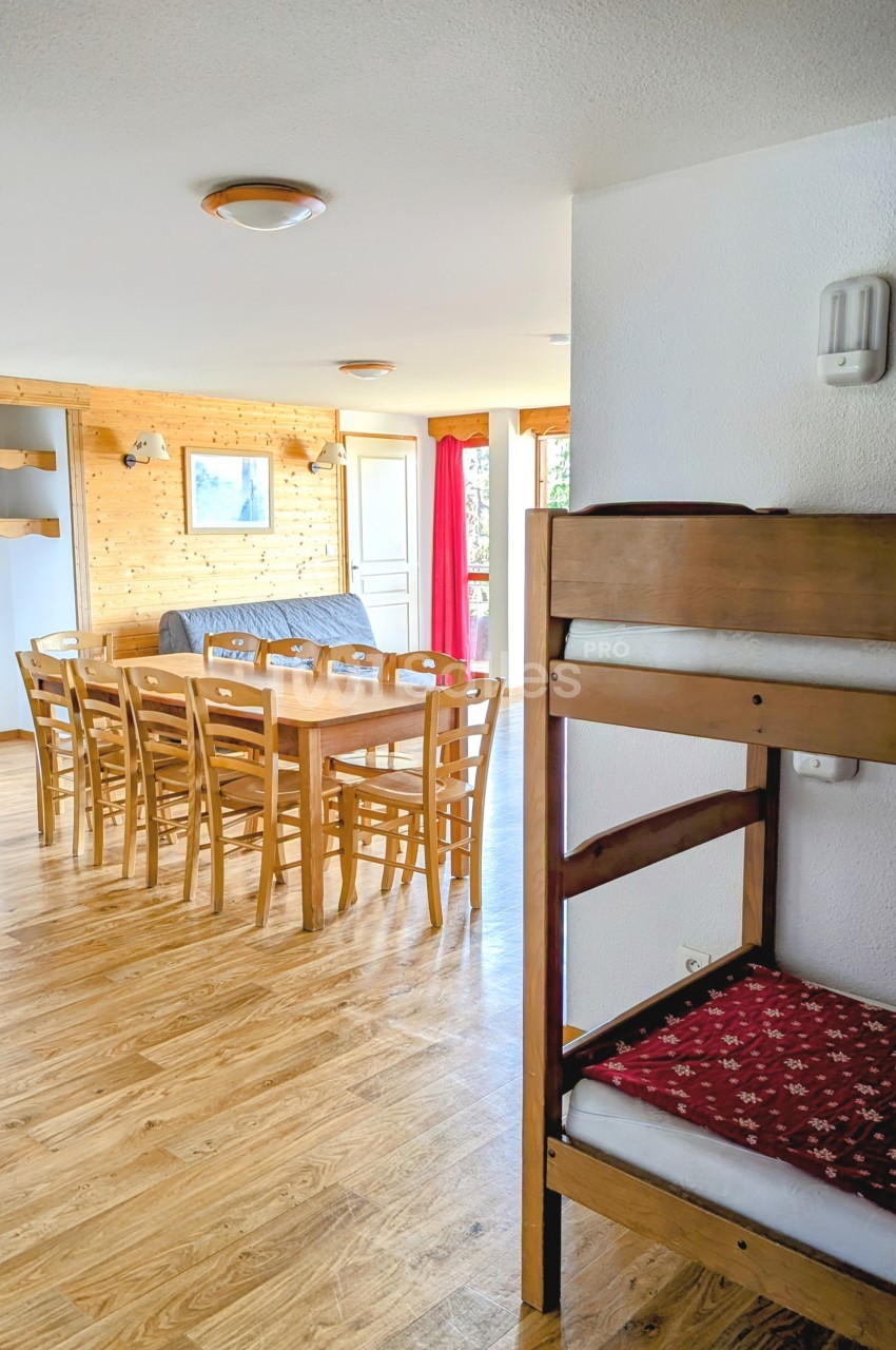 Salle à manger lumineuse avec table en bois, chaises assorties, canapé gris et lits superposés au premier plan.