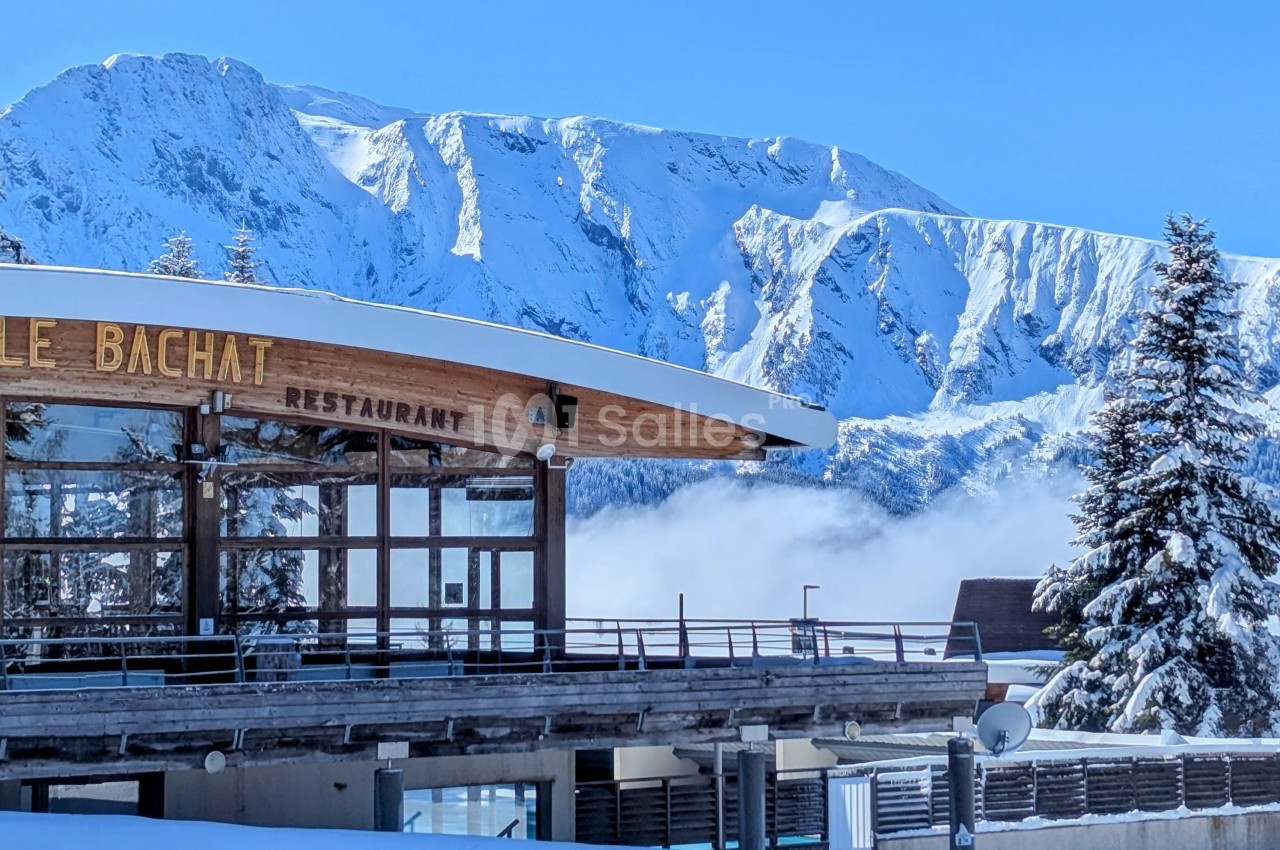 Façade d'un restaurant en bois avec montagnes enneigées en arrière-plan sous un ciel bleu.