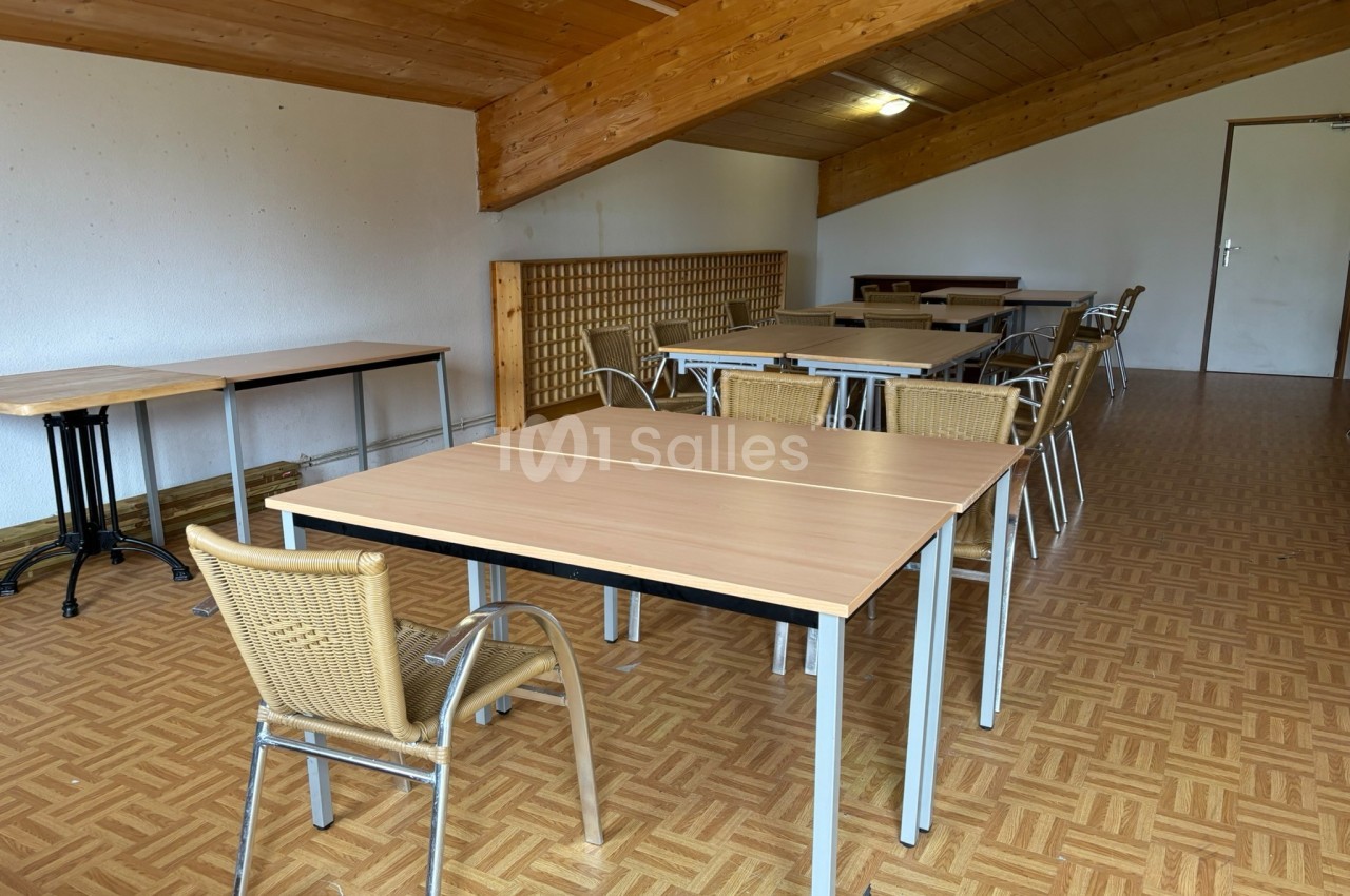 Salle avec des tables en bois clair, des chaises en osier et un plafond en bois incliné.