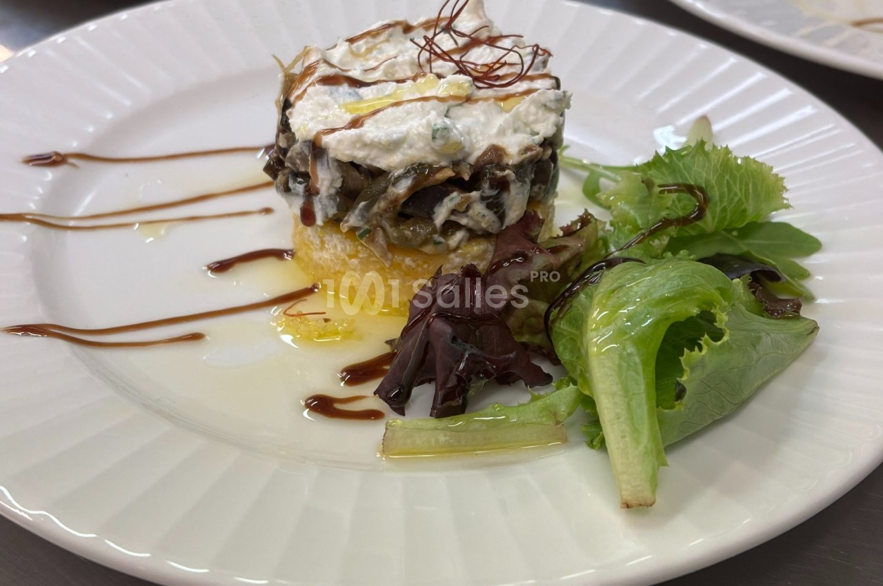 Assiette avec un millefeuille de légumes et fromage sur polenta, accompagné de salade verte et filet de sauce balsamique.