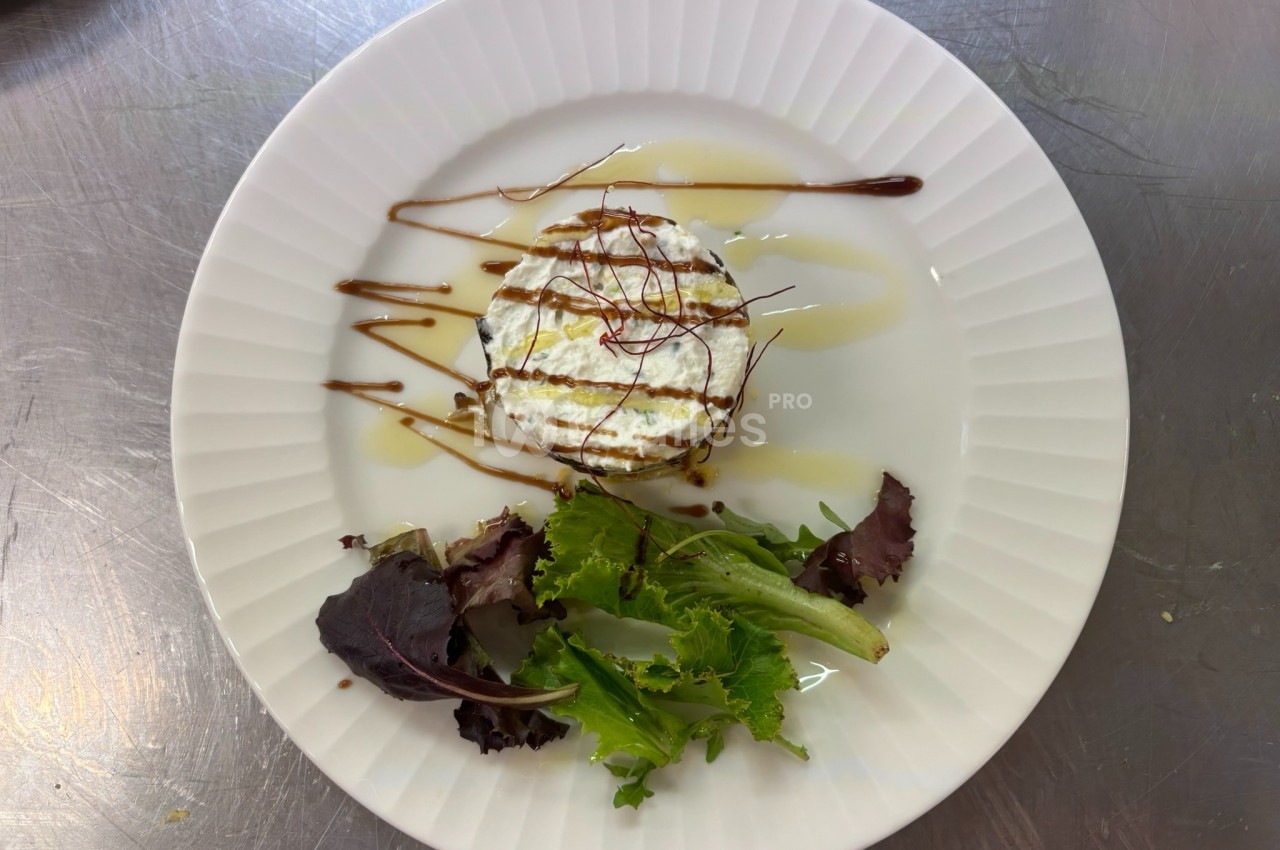 Assiette contenant un fromage frais garni de sauce, accompagné de jeunes pousses de salade.