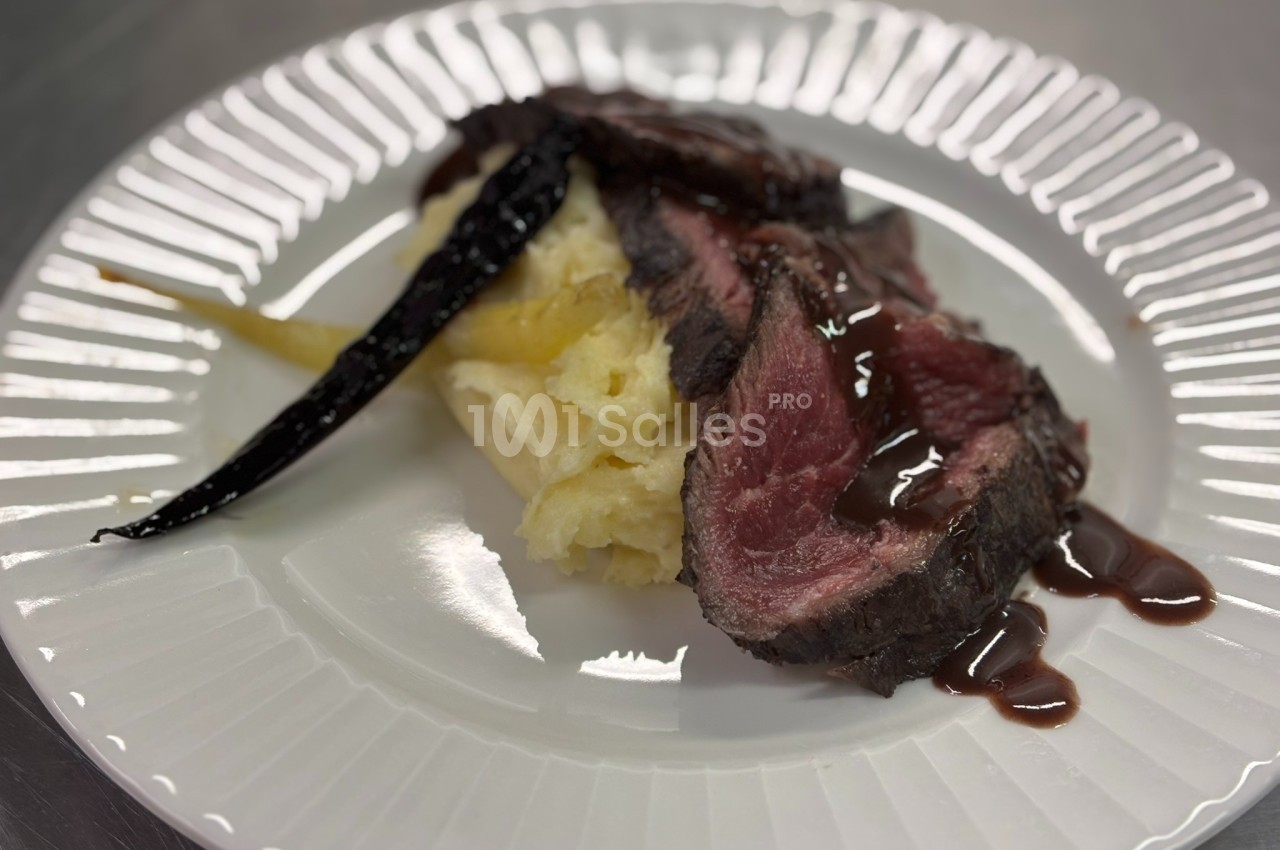 Assiette contenant une tranche de viande saignante, purée de pommes de terre et carottes glacées, nappée de sauce.