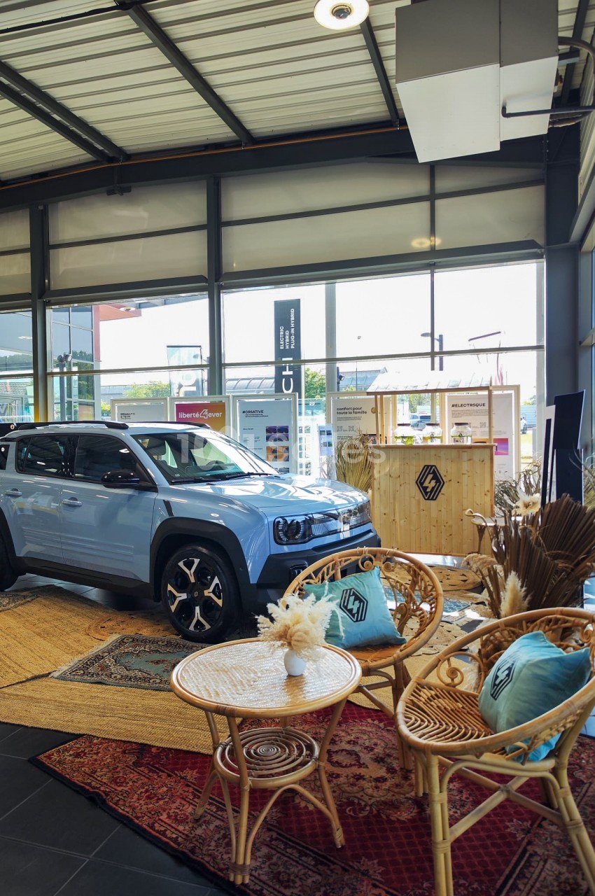 Un SUV bleu exposé dans un showroom lumineux, entouré de fauteuils en rotin et de décorations bohèmes.