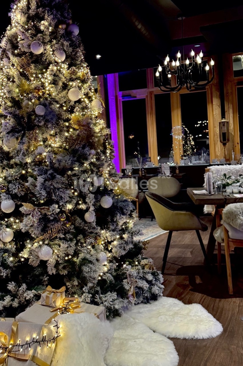Sapin de Noël décoré avec guirlandes lumineuses et boules, entouré de cadeaux, dans une salle à manger chaleureuse.