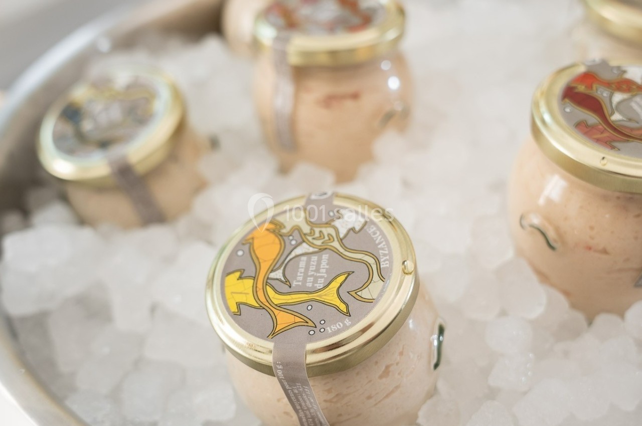 Pots de tartinade en verre avec couvercles dorés, posés sur de la glace pilée.