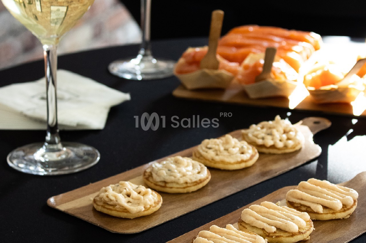 Assortiment de canapés au saumon et à la crème disposés sur des planches en bois, avec un verre de vin blanc.