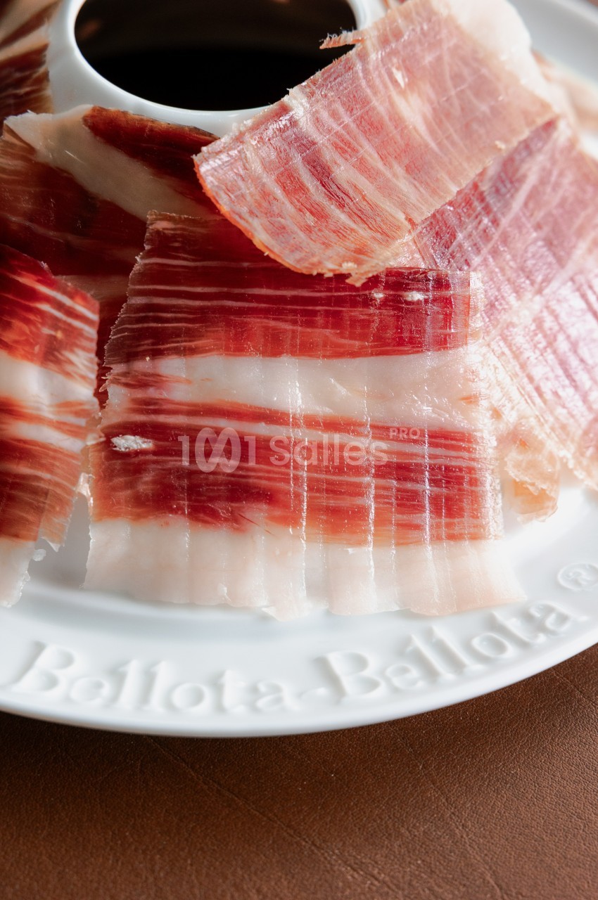 Tranches fines de jambon ibérique disposées en cercle sur une assiette blanche.
