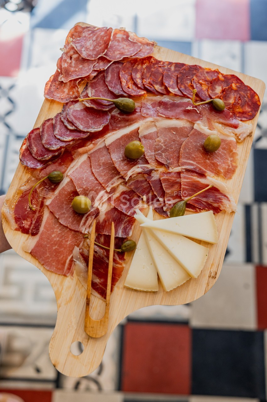 Plateau de charcuterie avec jambon, saucisson, chorizo, tranches de fromage et olives vertes sur une planche en bois.