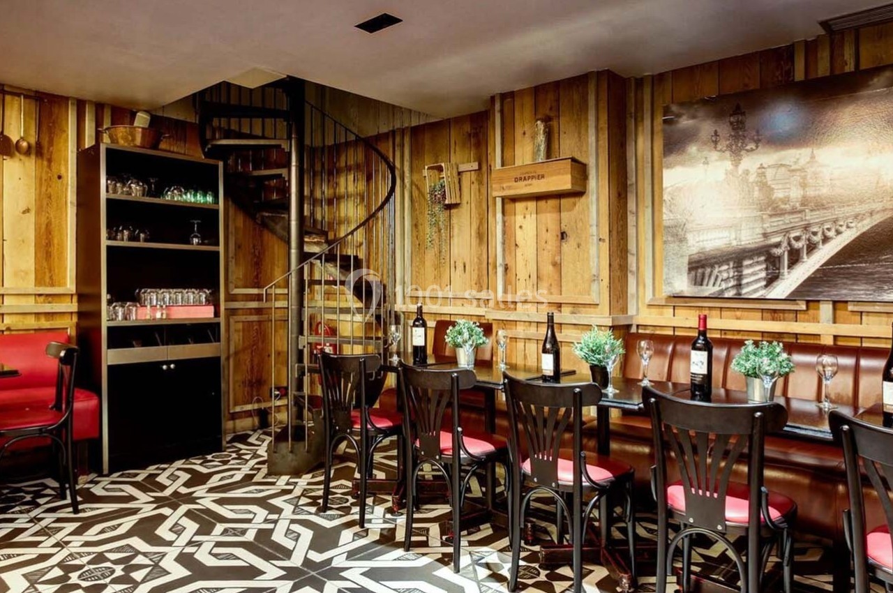 Salle de restaurant chaleureuse avec murs en bois, tables alignées, chaises noires et décoration murale en noir et blanc.