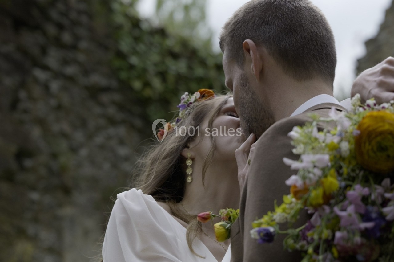 Un couple s'embrasse tendrement en extérieur, entouré de fleurs et de verdure.