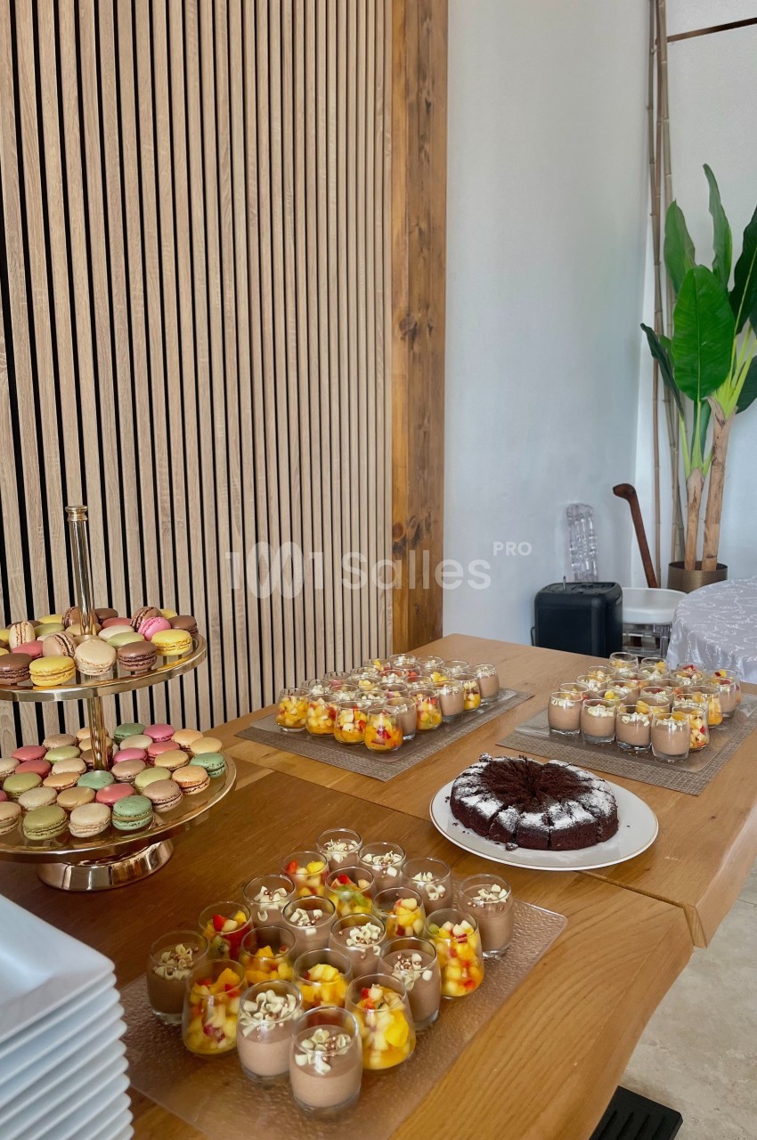Table en bois garnie de desserts variés, incluant macarons, verrines colorées et gâteau au chocolat.