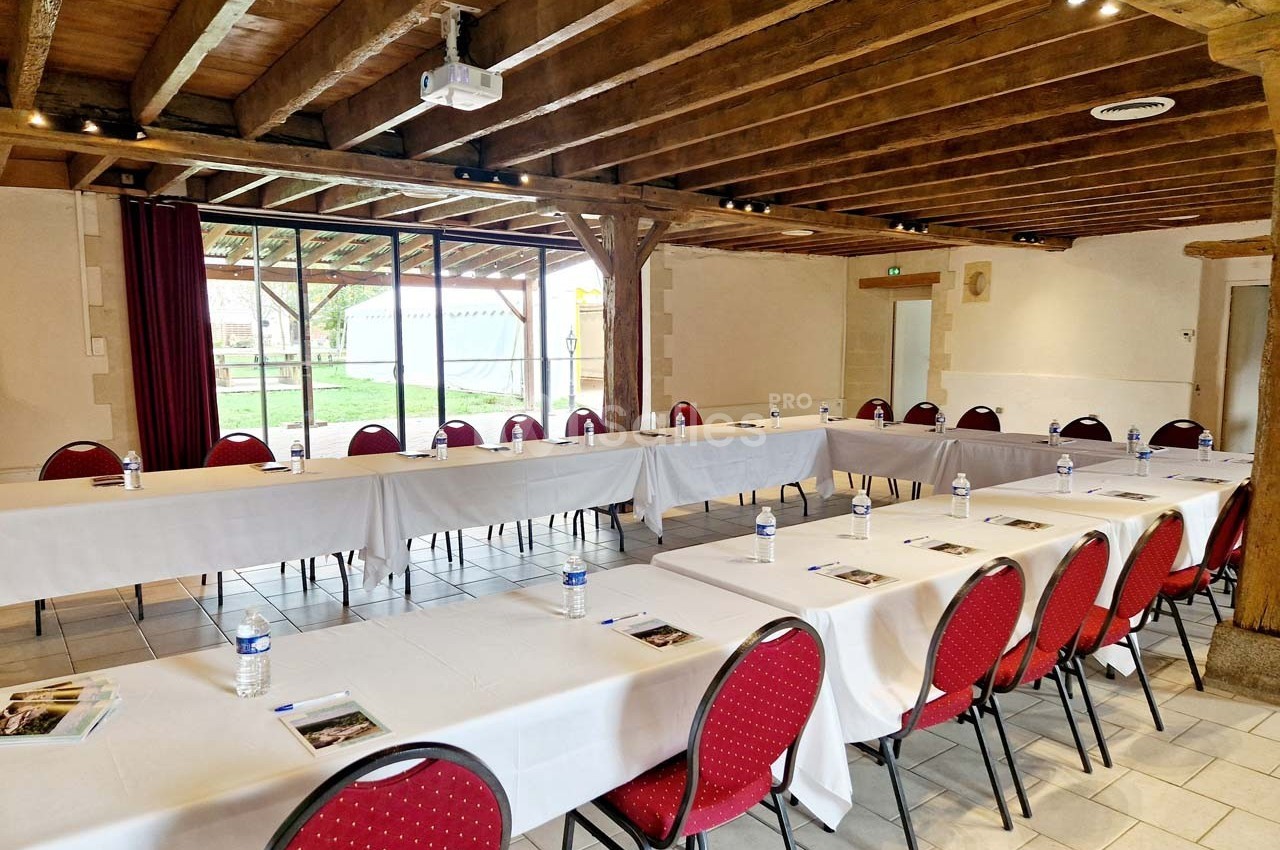 Salle de réunion lumineuse avec tables disposées en U, chaises rouges, bouteilles d'eau et documents sur chaque place.