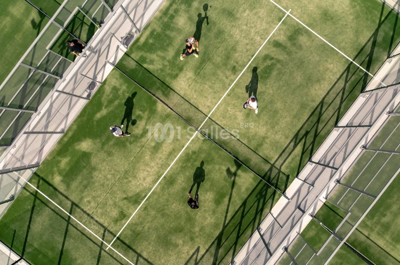 Vue aérienne de quatre personnes jouant au padel sur un terrain entouré de grillages.