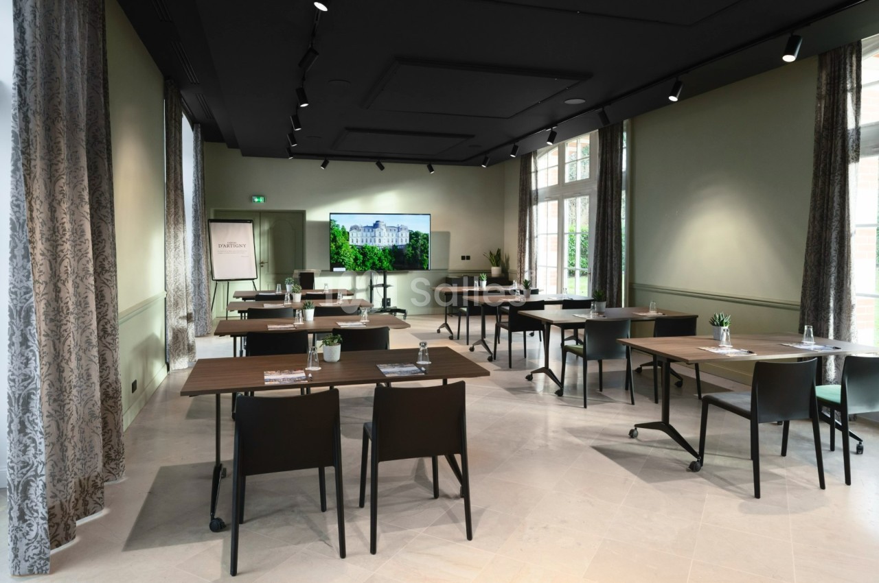 Salle de réunion lumineuse avec tables, chaises, écran de présentation et fenêtres donnant sur un espace vert.