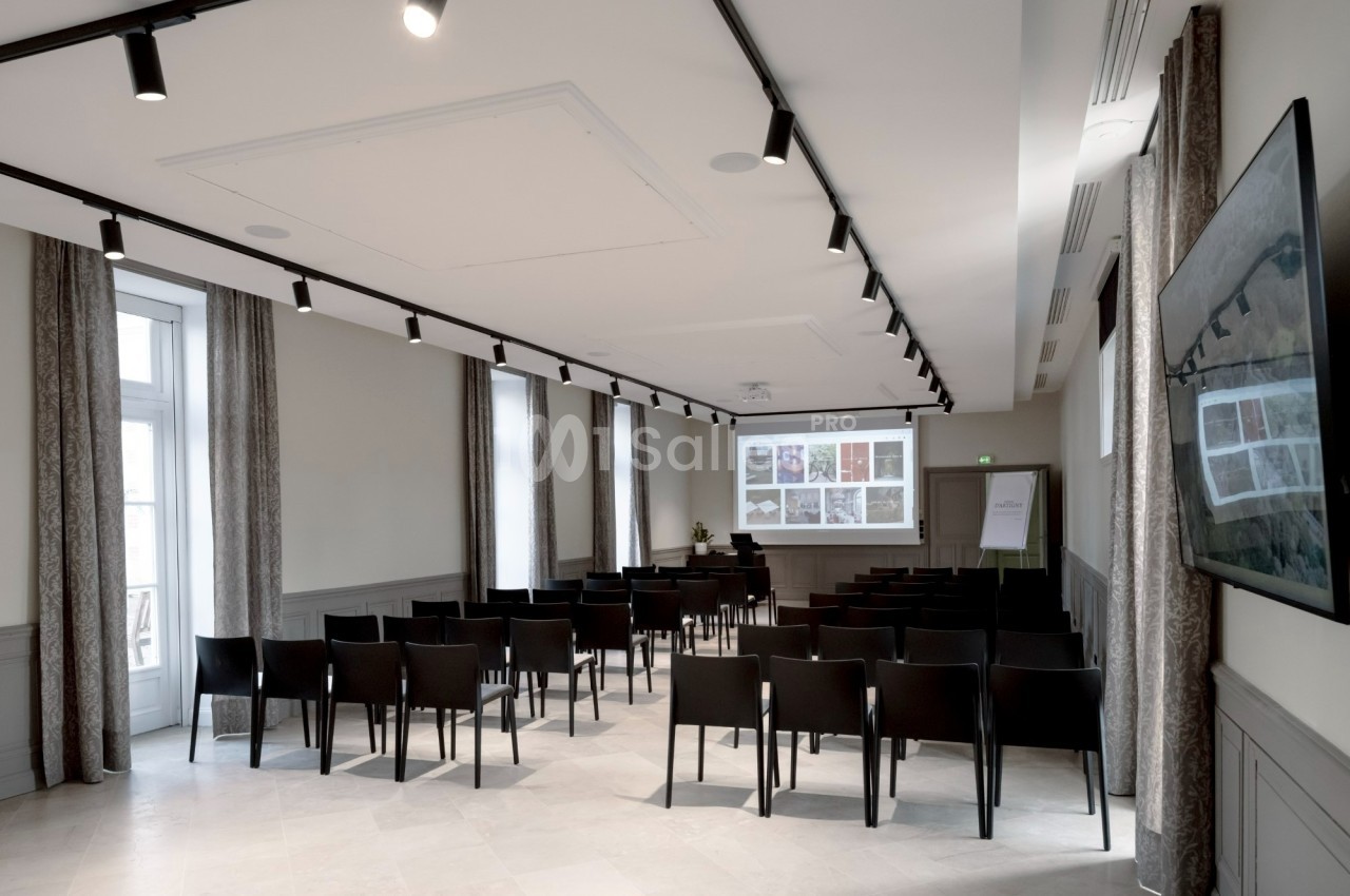 Salle de conférence lumineuse avec des chaises noires alignées, un écran de projection et un tableau de présentation.