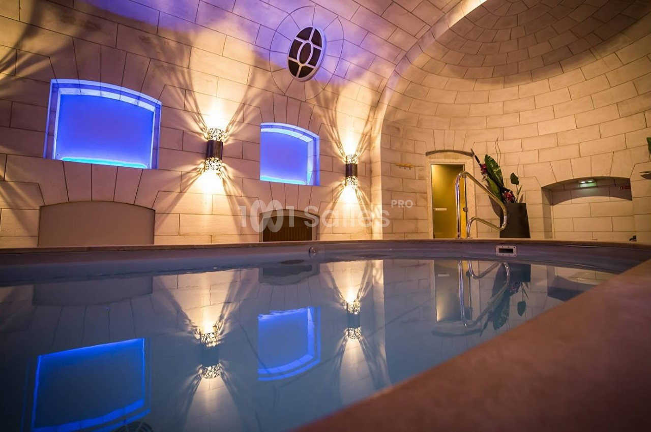 Piscine intérieure éclairée par des lumières bleues, entourée de murs en pierre et de plantes décoratives.