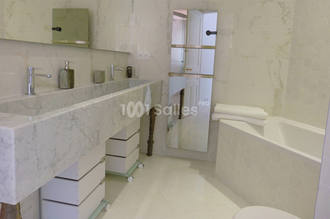 Salle de bain moderne avec lavabo double en marbre, baignoire, miroir et meubles de rangement blancs.