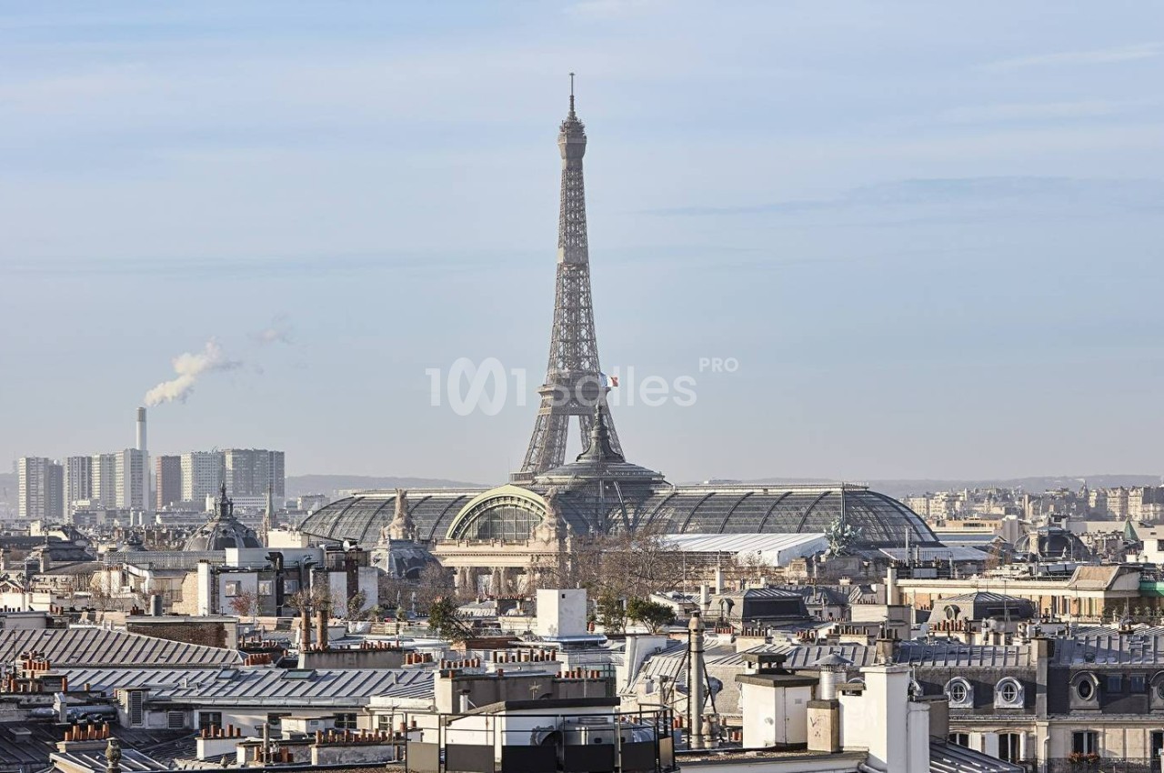 Vue sur les toits de Paris avec la tour Eiffel en arrière-plan et des bâtiments modernes à l'horizon.
