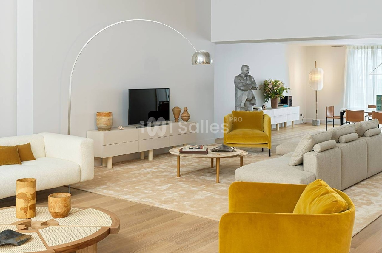 Salon moderne avec canapés clairs, fauteuils jaunes, table basse en bois, lampe arquée et décoration épurée.