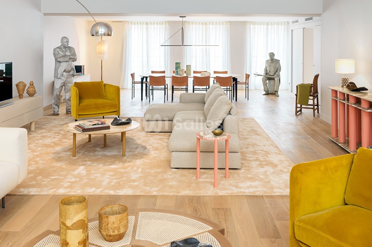 Salon spacieux et lumineux avec canapé beige, fauteuils jaunes, table basse, et sculptures décoratives.