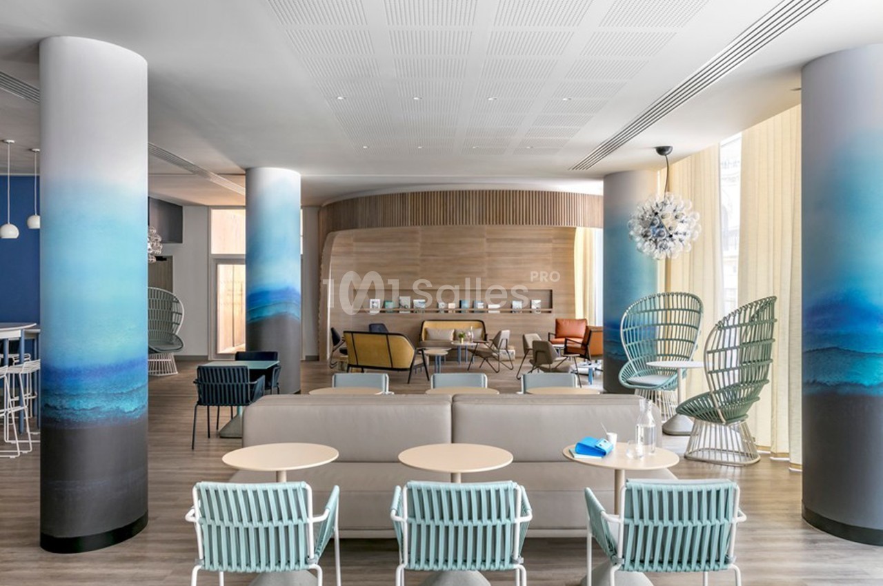 Espace lounge moderne avec fauteuils design, colonnes décorées de dégradés bleus et mobilier aux tons neutres.
