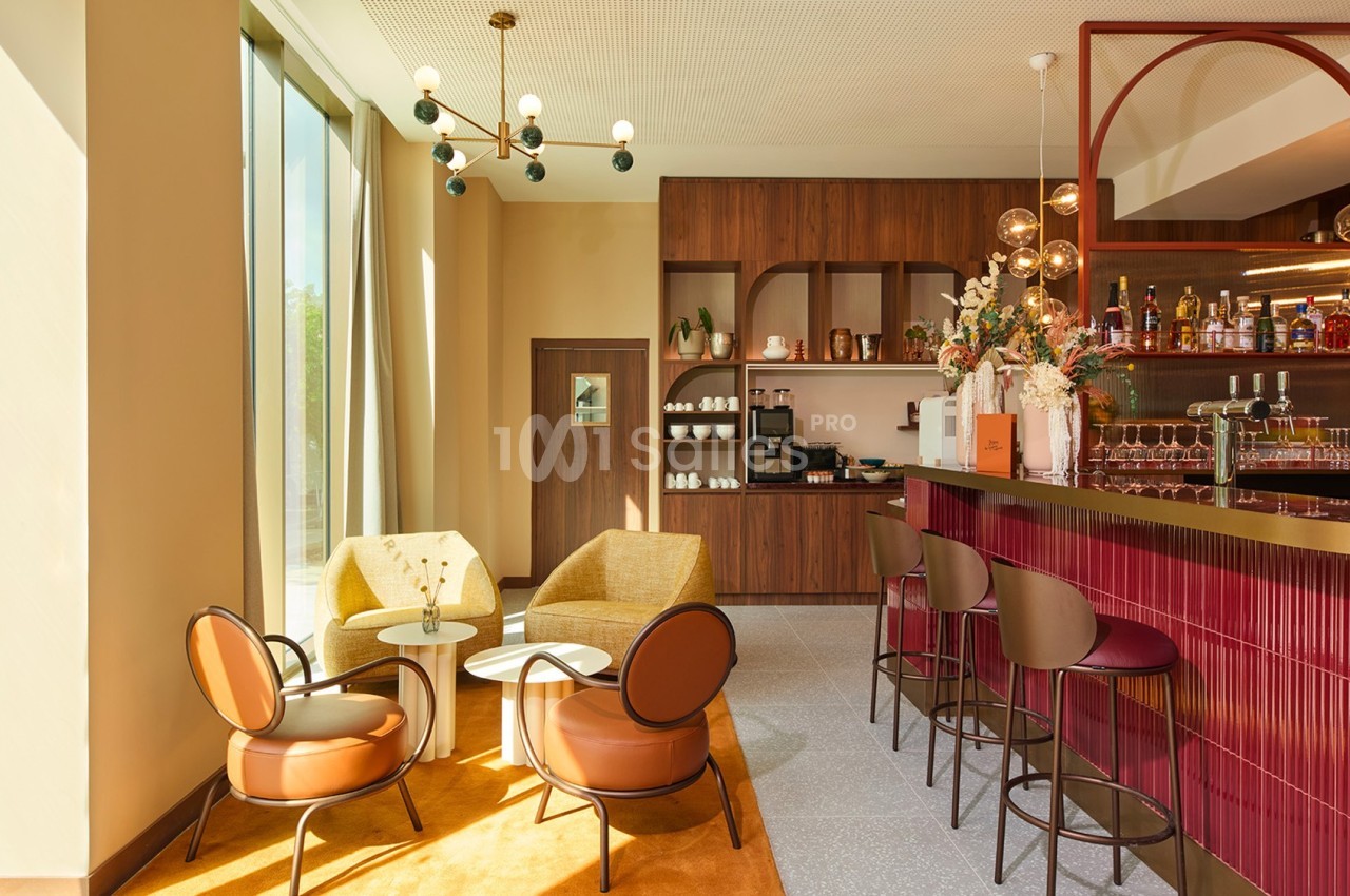 Espace lounge lumineux avec fauteuils, tables basses, bar en bois et étagères décoratives dans un décor moderne.