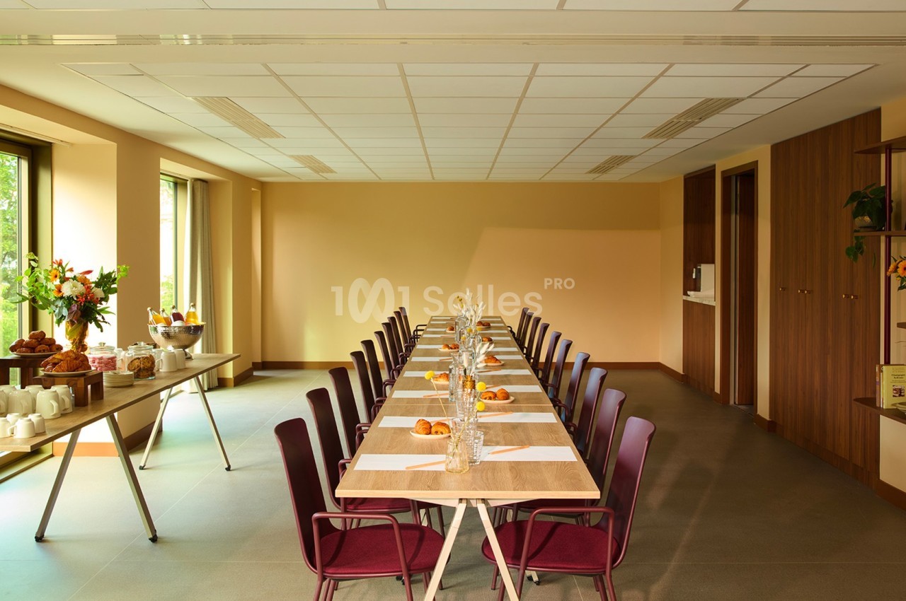 Salle lumineuse avec une grande table dressée pour un repas, entourée de chaises violettes, et un buffet sur le côté.