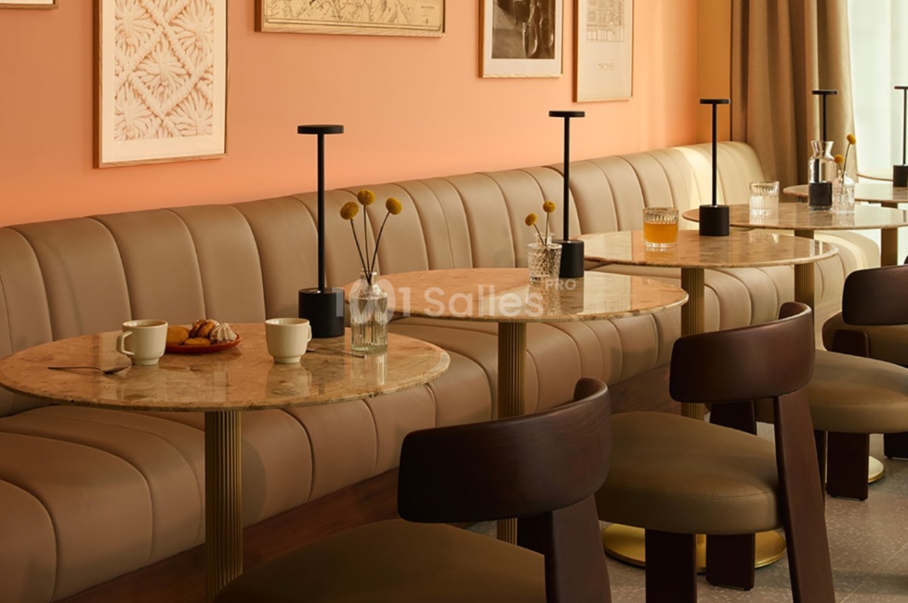 Banquettes en cuir beige et tables rondes en marbre dans un café à la décoration chaleureuse aux tons orangés.