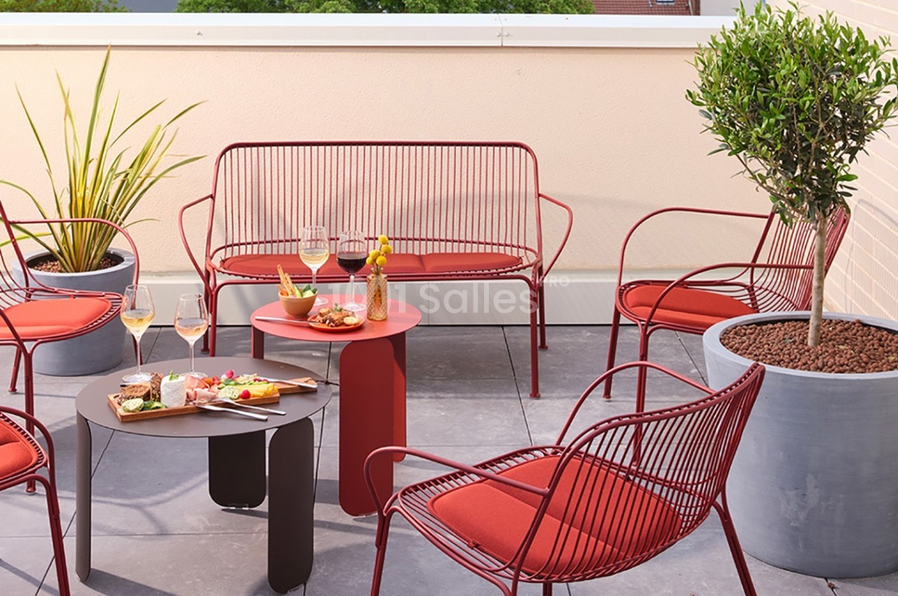Mobilier de jardin rouge avec table basse, apéritif servi, plantes en pot sur une terrasse ensoleillée.