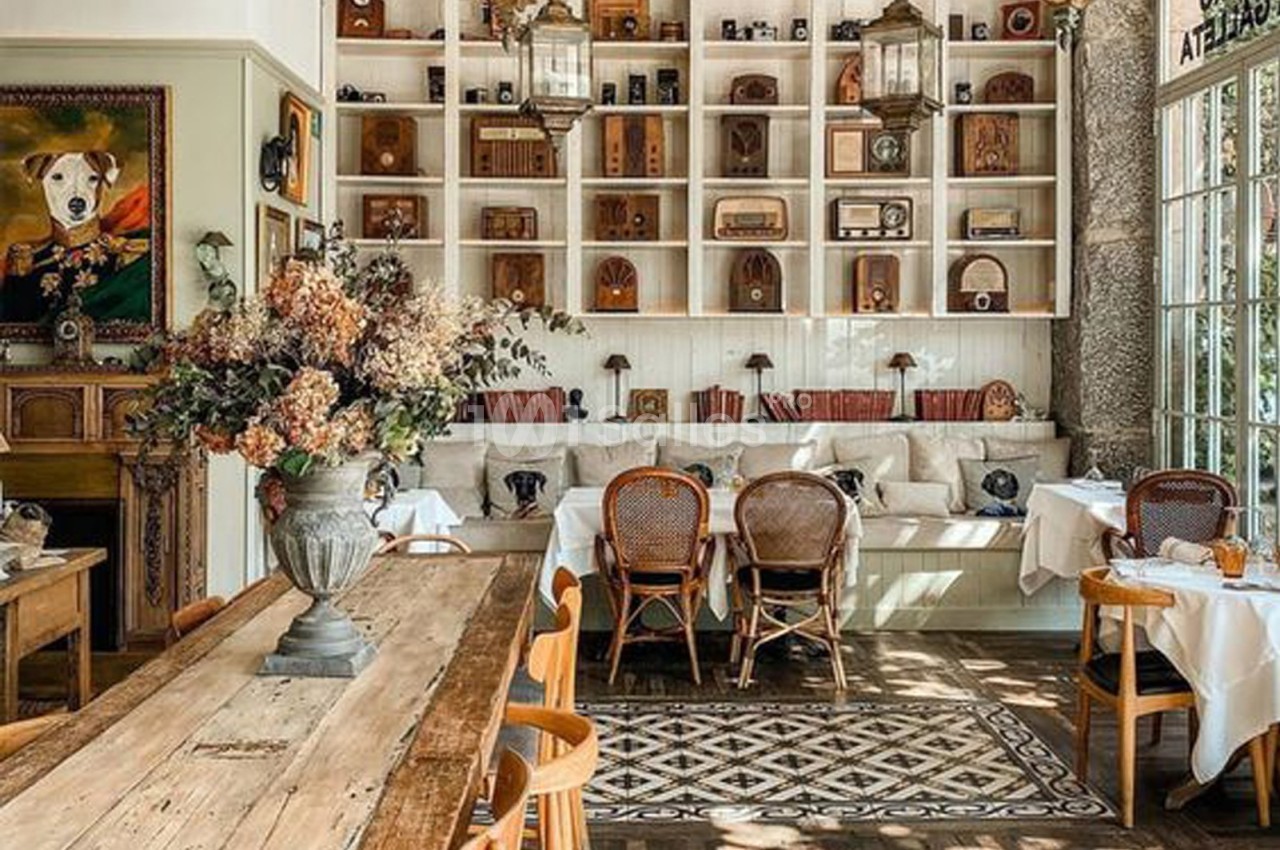 Salle lumineuse avec mobilier en bois, étagères décorées d'objets vintage, et tables dressées pour un repas.