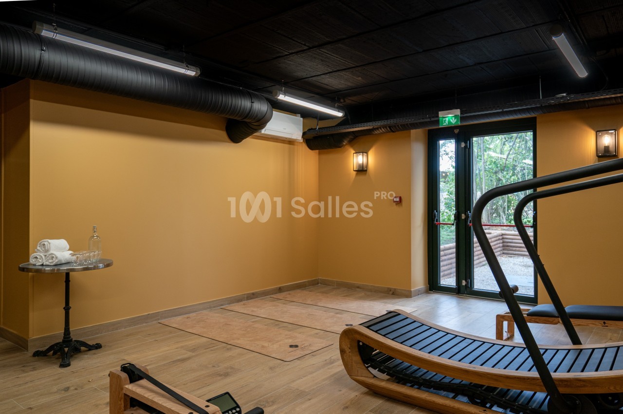 Salle de sport avec équipement en bois, murs orange, sol en bois, table avec serviettes et porte vitrée donnant sur l…
