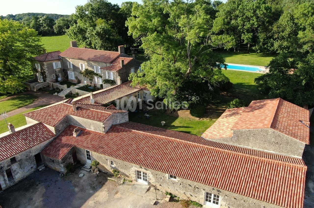 Vue aérienne d'un domaine avec bâtiments en pierre, toits en tuiles rouges, piscine et espaces verts environnants.