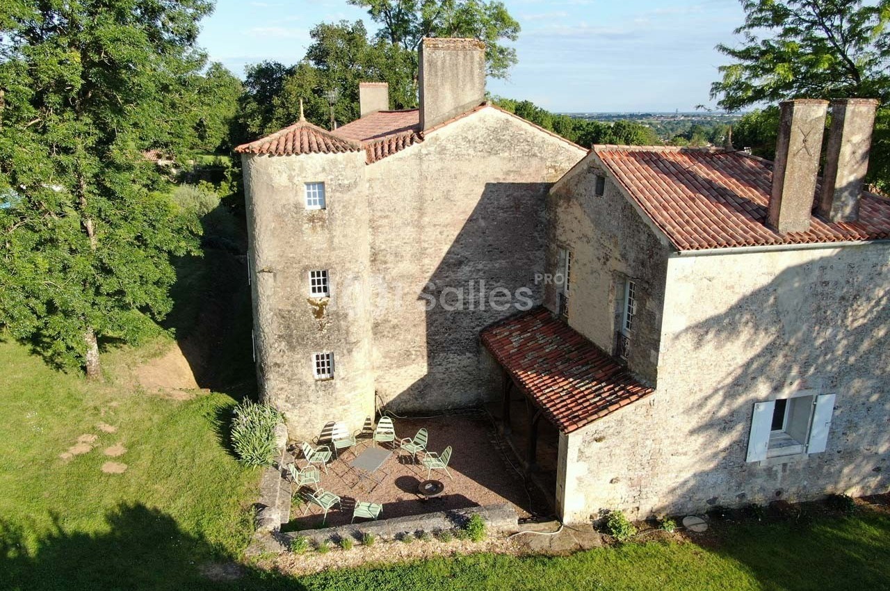 Cour d'une maison en pierre ancienne avec terrasse aménagée, entourée de verdure et d'arbres.