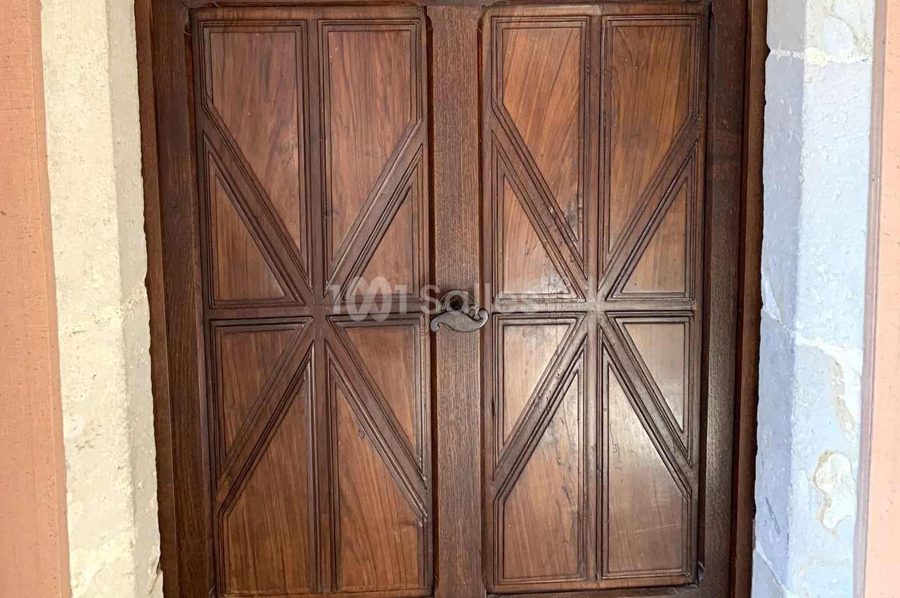 Porte en bois massif à deux battants avec motifs géométriques, encadrée de pierres claires.