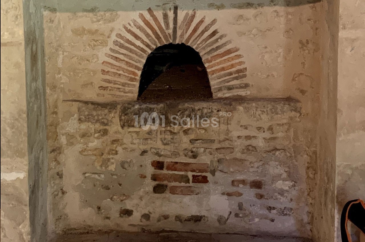 Ouverture voûtée en briques rouges dans un mur en pierre, probablement un ancien four ou une niche.