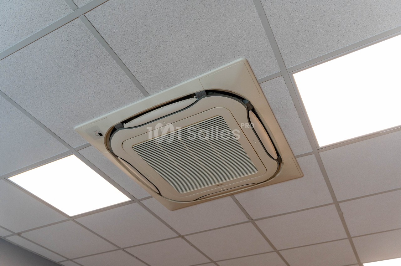 Un climatiseur encastré dans un plafond à dalles blanches, entouré de panneaux lumineux.