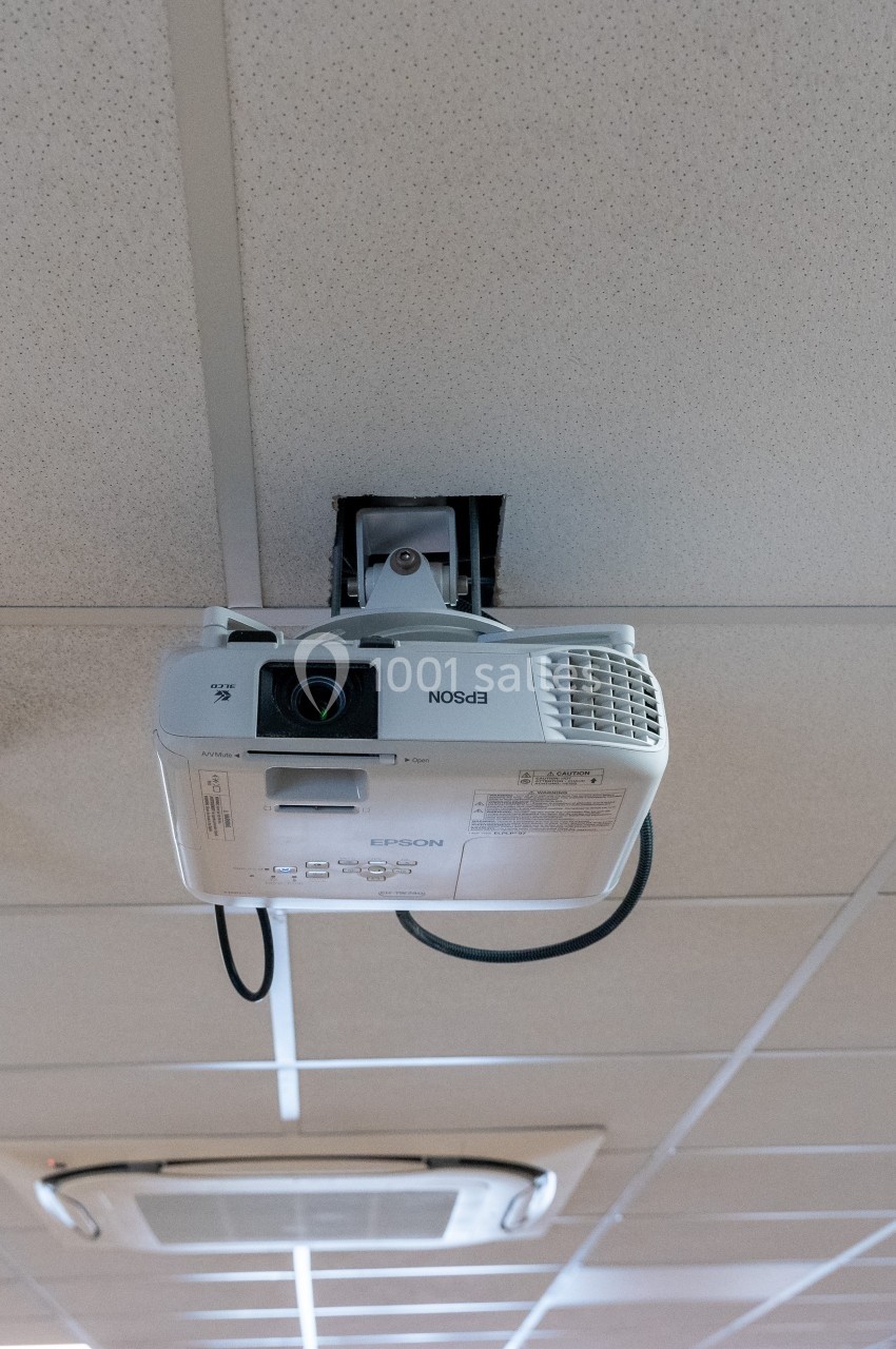 Projecteur suspendu au plafond d'une salle, orienté vers le bas, avec un câble connecté.