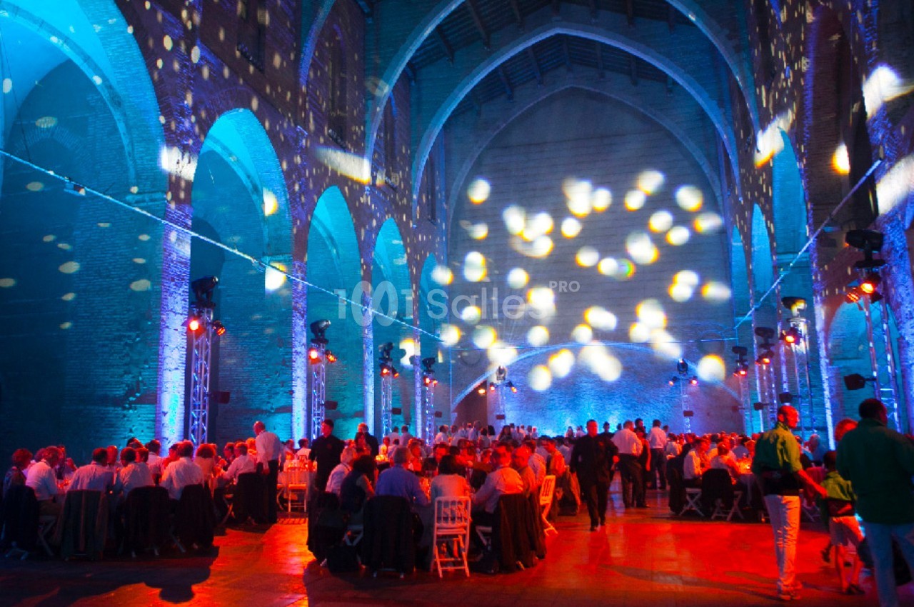 Salle voûtée illuminée par des projections colorées, avec des invités assis à des tables lors d'un événement.