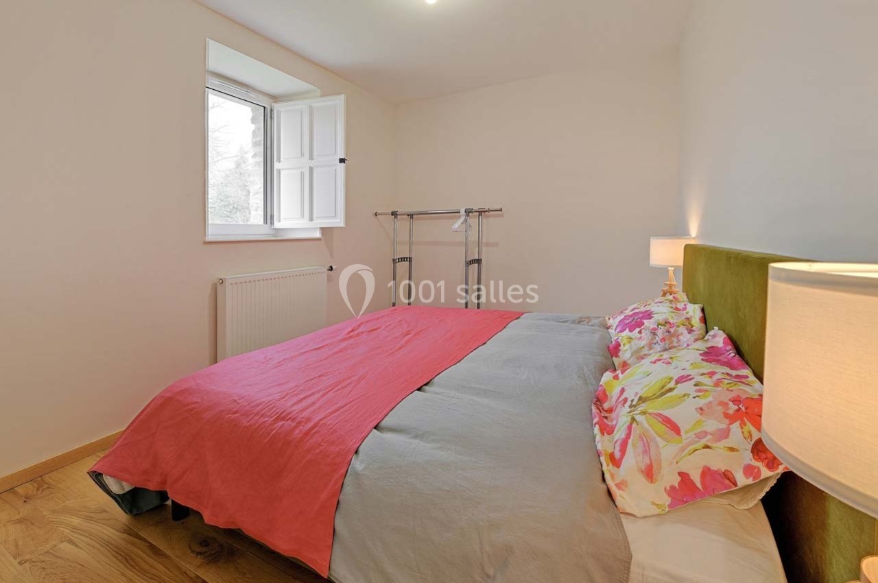 Chambre lumineuse avec un lit double, une parure colorée, un portant à vêtements et une fenêtre ouverte sur l'extérieur.