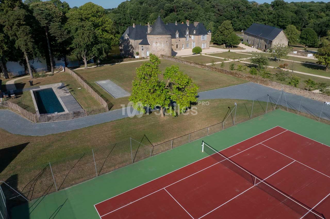 Vue aérienne d'un domaine avec un court de tennis, une piscine, des bâtiments en pierre et un parc arboré.