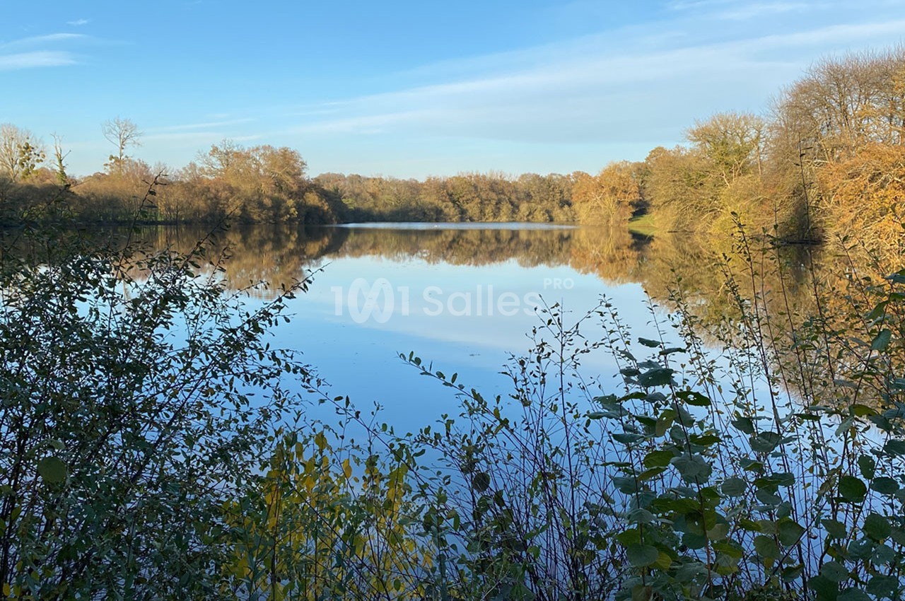 Vue d'un lac entouré d'arbres aux couleurs automnales, reflétés dans l'eau sous un ciel dégagé.
