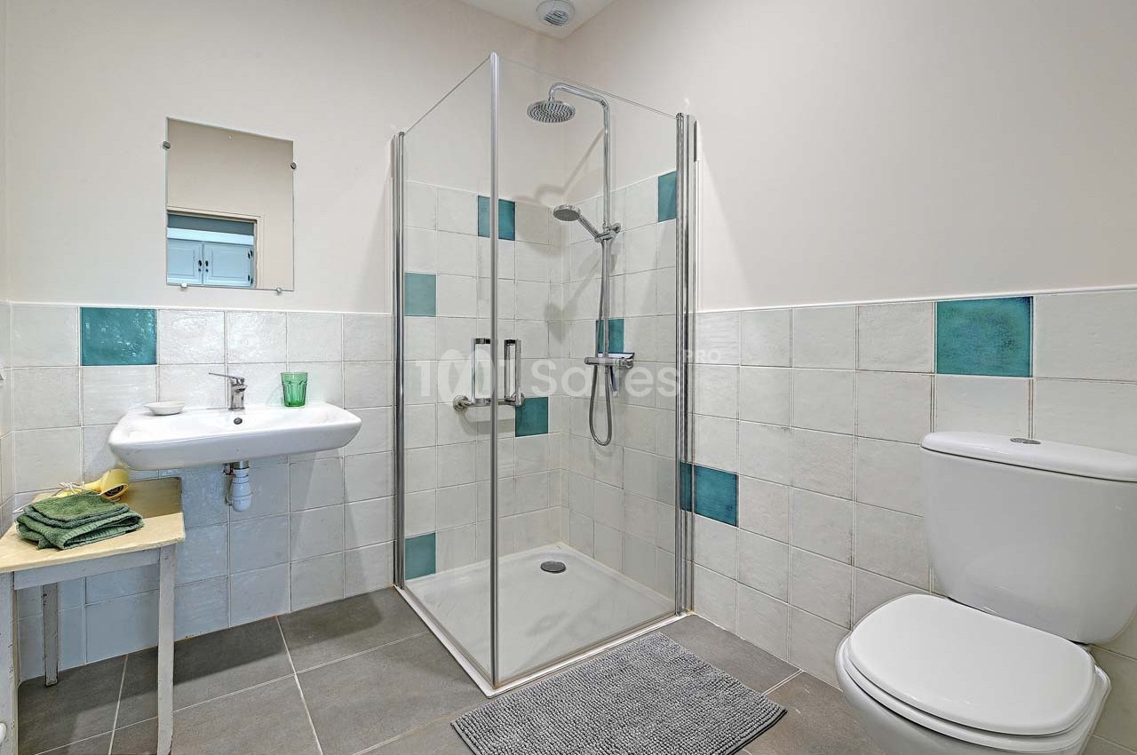 Salle de bain avec douche à l'italienne, lavabo, miroir, toilettes et carrelage blanc et turquoise.