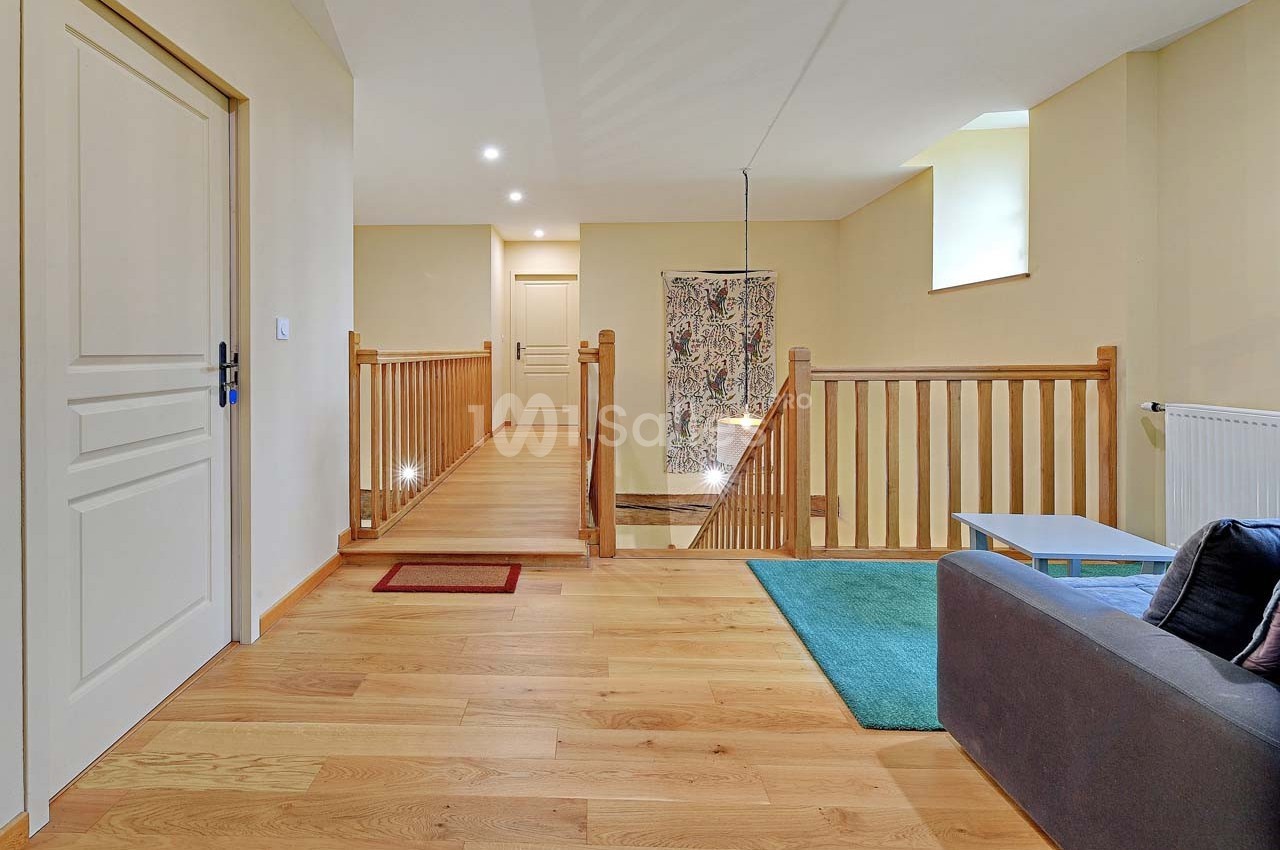 Vue d'un palier lumineux avec parquet en bois, garde-corps en bois, canapé gris et tapis vert.