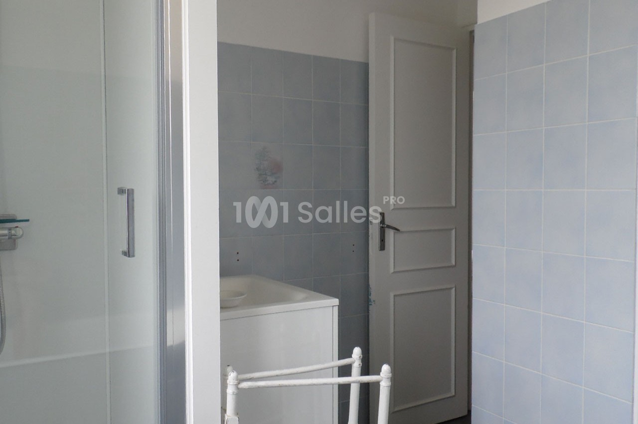 Salle de bain avec murs carrelés bleus, porte blanche ouverte et cabine de douche partiellement visible.